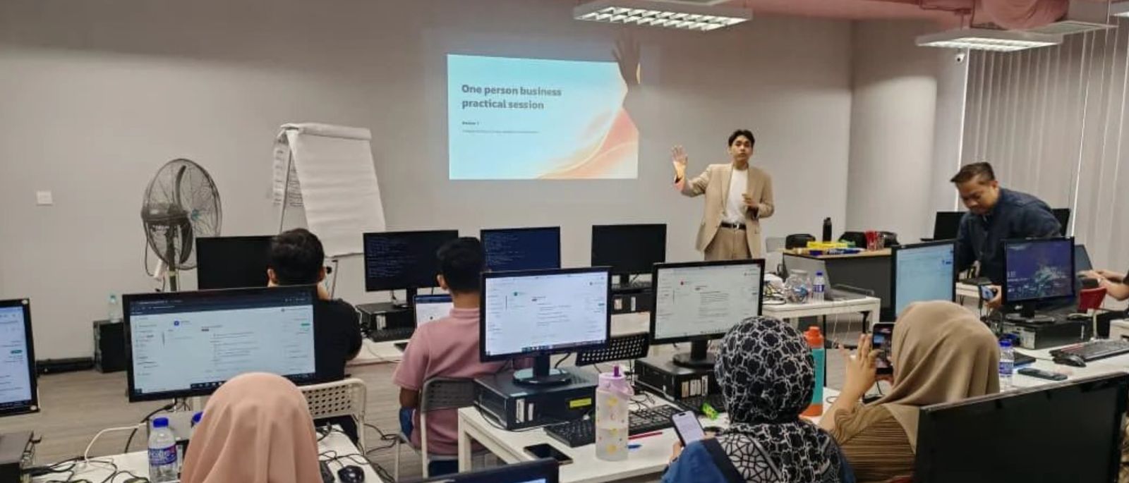 Coach Kaio teaching a hands-on session in a computer lab, participants working at their own screens